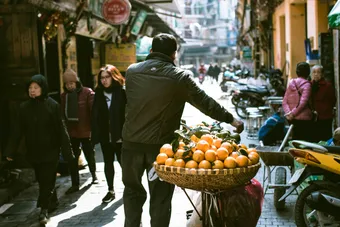 A busy street scene in Hanoi with a vendor selling fresh oranges. Fruits are pretty delicious in Vietnam.
