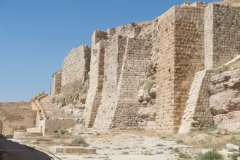 Stone ramparts of a medieval fortress overlooking an arid landscape under a blue sky