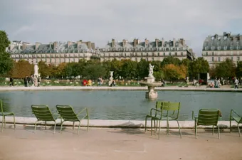 The statue-lined paths open onto the central basin of this famous Parisian garden in the 6th arrondissement, where green chairs invite visitors to sit and admire the formal French gardens. Golden light glides across the Palais's facade and makes the fountains sparkle, giving the park an almost theatrical charm.