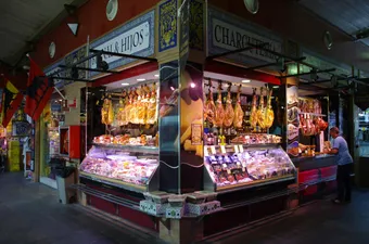 Étal de charcuterie traditionnelle au Mercado de Triana, célèbre marché couvert de Séville, avec ses jambons ibériques suspendus et ses spécialités andalouses.