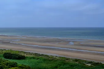 Tranquil view of Omaha Beach in France, showcasing vast sand and calm sea under blue skies