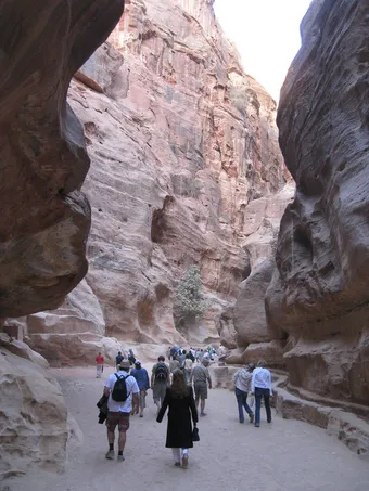 Visitors walking through Petra’s Siq, a narrow sandstone canyon with high rock walls