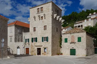 View of the village of Pučišća, renowned for its finely cut white stone houses, here dominated by a traditional tower with green shutters. The scene conveys a peaceful, authentic atmosphere typical of Dalmatian villages on the island of Brač.