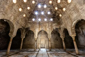 Salle du Bañuelo de Grenade, l’un des bains arabes les mieux conservés d’Espagne, datant du XIᵉ siècle et témoignant de l’importance des hammams dans la vie sociale de l’Andalousie musulmane. L'architecture est typique d'un hammam andalou d’époque islamique avec : une voûte en briques percée d’ouvertures étoilées pour laisser passer la lumière, des arches en plein cintre reposant sur des colonnes, une grande salle rectangulaire typique des salles chaudes ou tièdes des bains publics.