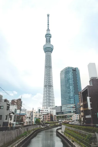 The Tokyo Skytree rises above the city and dominates the urban skyline. It can be seen from the canal, framed by modern buildings and residential areas.