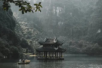 Serene scene of a traditional pagoda on the Tam Coc river in Ninh Bình, surrounded by lush greenery.