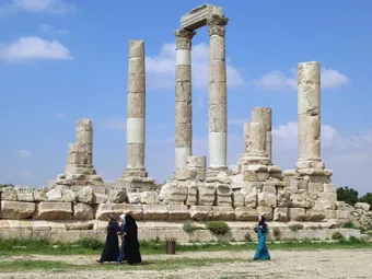 Roman ruins with stone columns at an archaeological site, with visitors walking in the foreground.