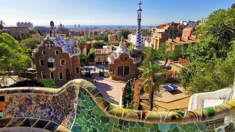 Panoramic view of Park Güell in Barcelona featuring Gaudí’s modernist houses, colorful mosaics, and the city skyline in the background