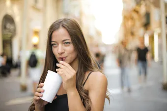 Woman sipping a beverage outdoors in a sunny city street, embodying leisure and enjoyment
