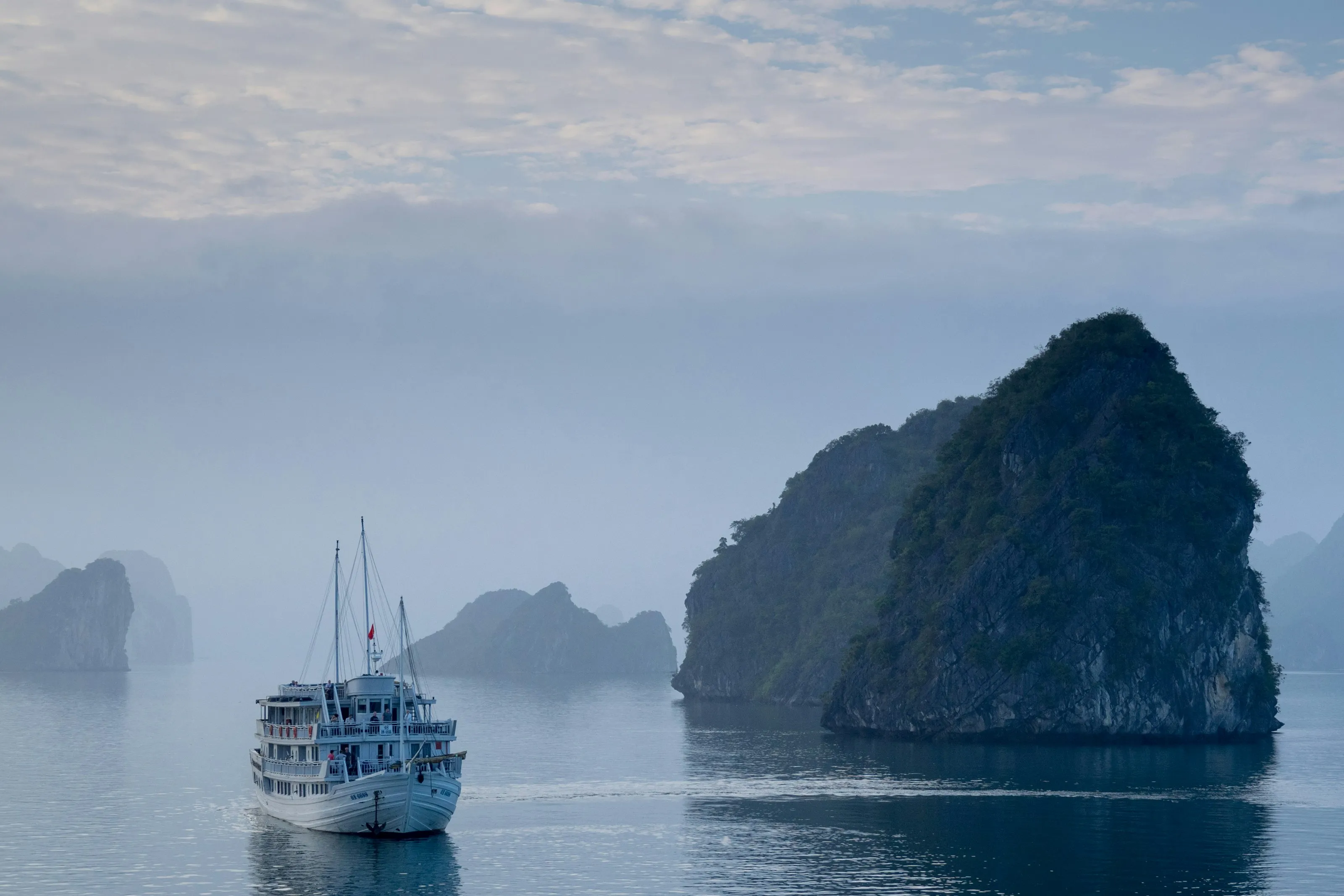 A white ship in Ha Long Bay near a rock formation covered with grass and trees